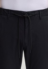 Czarne spodnie z elastycznym pasem i sznurkiem, z zapięciem na guziki z przodu, gładką bawełnianą tkaniną i bocznymi kieszeniami.