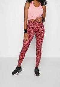 Różowy top sportowy połączony z legginsami o wysokim stanie w czerwony leoparda, charakteryzujący się gładką fakturą i czarnymi akcentami logo Nike.