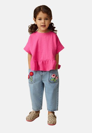 Rosa Kurzarmoberteil mit Rüschensaum, hellblaue Jeanshose mit floralem Stickerei an den Taschen und Halbschuhe mit Leopardenmuster.