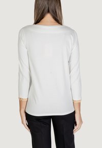 Top bianco a maniche lunghe con maniche a tre quarti, caratterizzato da dettagli in pizzo ai polsini e da un collo rotondo, abbinato a pantaloni neri.