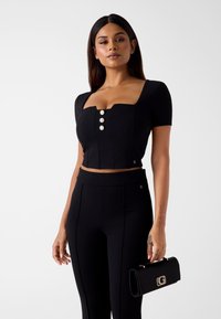 Czarny krótki top z krótkimi rękawami, kwadratowym dekoltem i trzema dekoracyjnymi guzikami. Uzupełniony czarnymi spodniami z wysokim stanem i kopertówką.