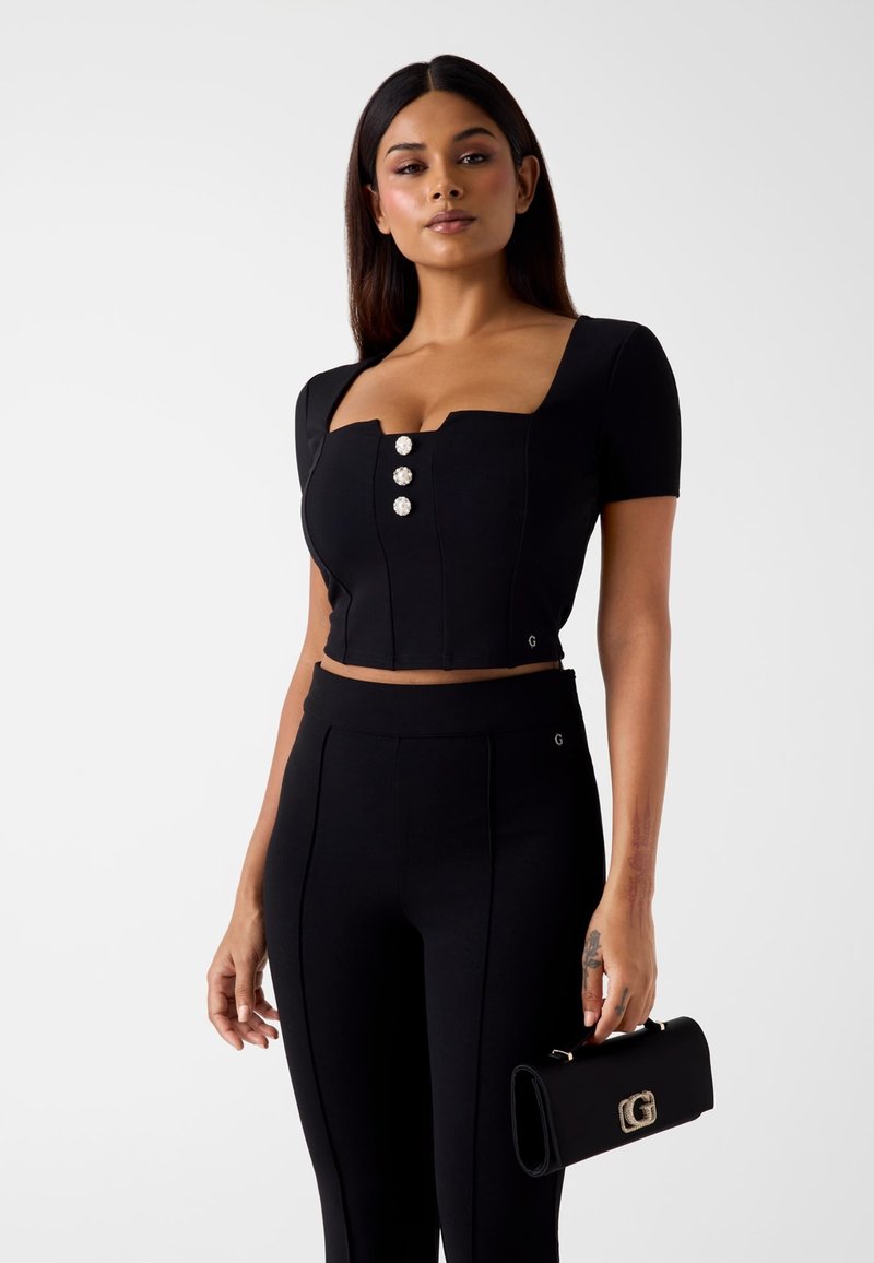 Czarny krótki top z krótkimi rękawami, kwadratowym dekoltem i trzema dekoracyjnymi guzikami. Uzupełniony czarnymi spodniami z wysokim stanem i kopertówką.