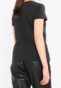Černé bavlněné tričko s krátkými rukávy a kulatým výstřihem, spojené s černými kalhotami z umělé kůže. Hladká textura, přiléhavý střih.