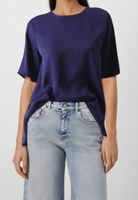 Marinebluse aus Satin mit kurzen Ärmeln und rundem Ausschnitt, kombiniert mit hellblauen, hoch taillierten Jeans im klassischen Fünf-Taschen-Design.