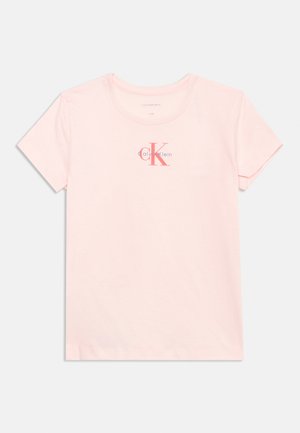 Osvetljeno roza kratka majica s kratkimi rokavi s Calvina Kleina logotipom v rdeči in mornarsko modri barvi na sredini prsnega koša, enobarvna podlaga.