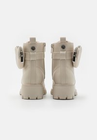 Stivaletti beige alla caviglia con suola robusta, dotati di tasca con zip e dettagli con nastro, materiale sintetico liscio e tallone rinforzato.