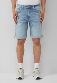 Shorts en jean bleu clair avec des ourlets retroussés, cinq poches et une fermeture à bouton à l'avant. Portés avec des chaussettes blanches et des baskets claires.