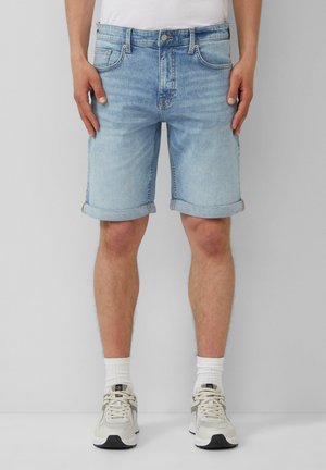 Lichtblauwe spijkershorts met opgerolde zomen, vijf zakken en een knoopsluiting aan de voorkant. Gekocht met witte sokken en lichtgekleurde sportschoenen.