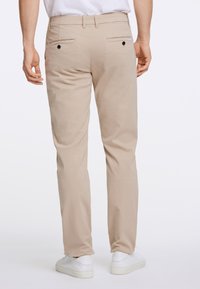 Bēšas krāsas chinos bikses ar aizmugurējām kabatām un pogu aizdares, taisnas kājas dizains. Savienots ar baltām sporta kurpēm.