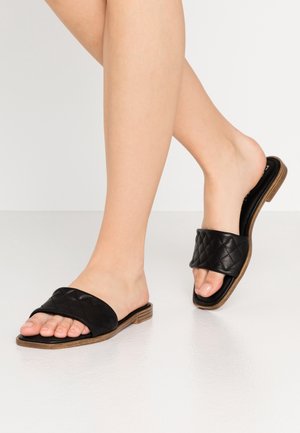 Mules noires matelassées avec un design à bout ouvert, dotées d'une semelle en bois élégante et d'une bride texturée pour un détail supplémentaire.