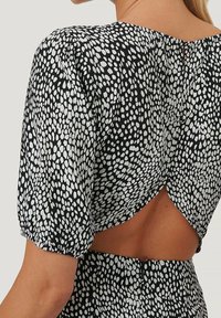 Un vestido estampado en blanco y negro con un diseño recortado, mangas abullonadas y un respaldo abierto, que muestra una textura suave y un cierre con botones.