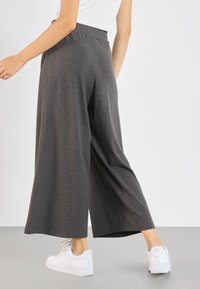 Pantalon gris à jambes larges avec motif à fines rayures, taille élastique et texture douce, accompagné de baskets blanches.