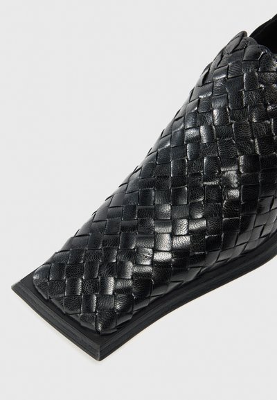 Scarpa slip-on in pelle intrecciata nera con punta a punta e suola piatta, caratterizzata da una texture liscia e un distintivo motivo intrecciato.