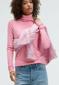 Pink turtleneck sweater in soft fabric, paired with a textured light pink knit scarf. Model also wears light blue denim jeans.