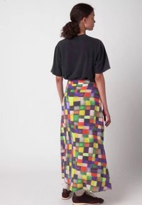 Maxi-rok met een levendig patchworkpatroon in kleuren zoals groen, oranje en paars, gemaakt van lichtgewicht stof. Gecombineerd met donkere sneakers.