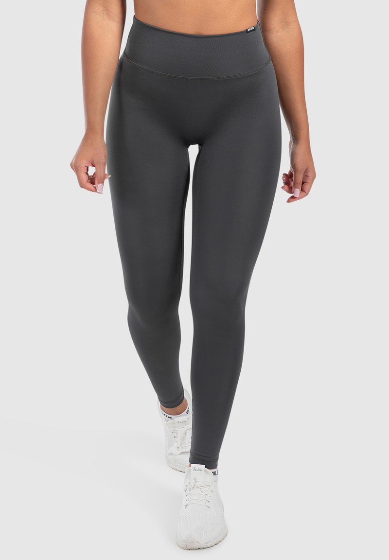 Leggings a vita alta, aderenti, di colore grigio scuro, realizzati in un materiale liscio e elasticizzato. Accentuati da un logo del marchio minimalista in vita.