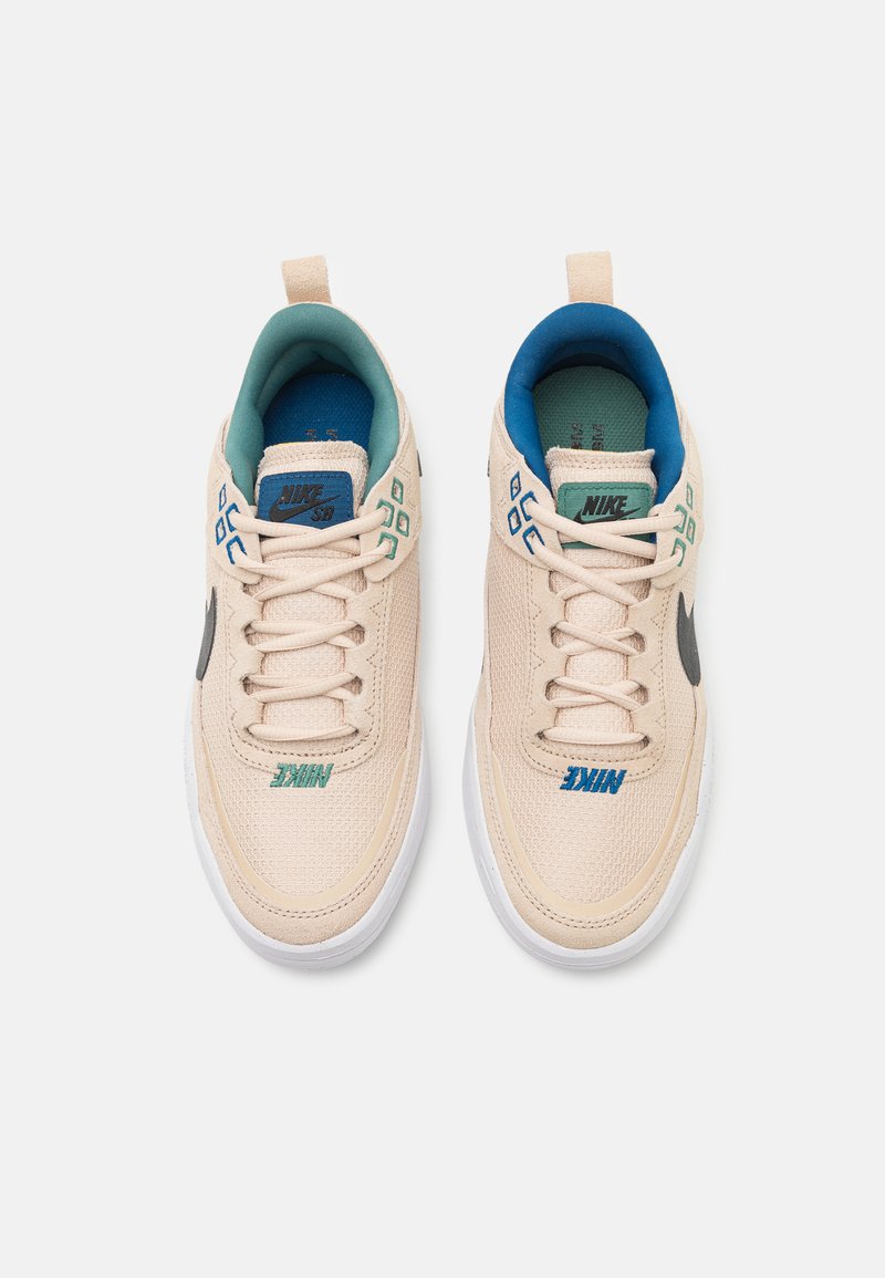 Beige Sneaker mit Mesh-Obermaterial und weißer Gummisohle. Mit blauen und grünen Akzenten; Logo auf der Zunge und der Seite, Schlaufen an der Ferse für einfaches Anziehen.