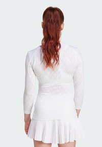 White athletic dress with long sleeves, textured diamond pattern, pleated skirt, and fitted bodice. Smooth fabric with a lightweight feel.