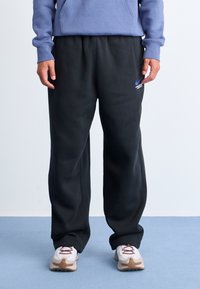 Svarte joggebukser med elastisk midje, sidelommer og en blå Nike-logo. Kombinert med hvite joggesko med vinrøde detaljer.