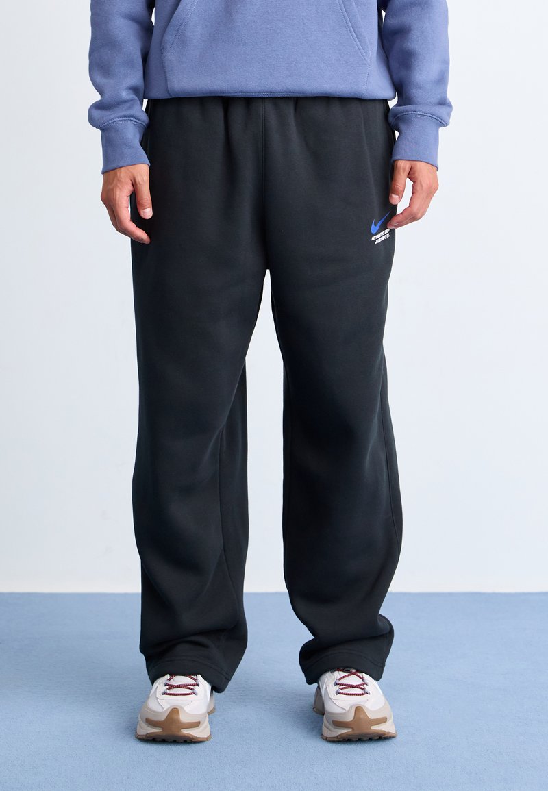 Pantalons de survêtement noirs avec taille élastique, poches latérales et logo Nike bleu. Assortis à des baskets blanches avec des accents bordeaux.