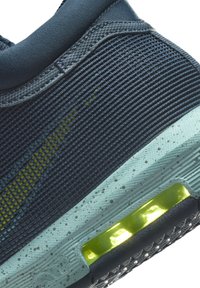 Gros plan sur une chaussure de sport bleu marine avec un tissu texturé, une semelle intermédiaire bleu clair tachetée et un détail de coussin d'air jaune néon.