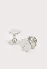 Silverfärgade cufflinks med en polerad yta, prydda med ingraverad branding. Rund form med en slät textur och en klassisk design.