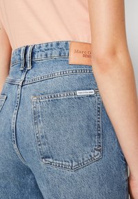 Jeans de mezclilla azul de cintura alta con una placa de cuero de la marca, que presentan un diseño clásico de cinco bolsillos y detalles de costura en contraste.