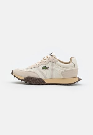 Lacoste Sneakers in Beige und Creme, mit einer strukturierten Oberfläche, Schnürdesign, grünem Logo und brauner Gummisohle mit Noppen.