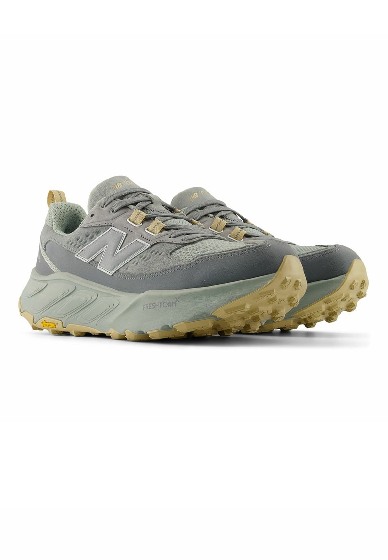 Paire de chaussures de trail running New Balance grises et beiges avec semelles texturées et semelles intermédiaires Fresh Foam, présentées en biais sur un fond blanc.