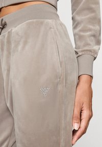Lyse beige joggebukser laget av myk fløyel, med en sidelomme og en liten krystallprydet trekantlogo på venstre lår.