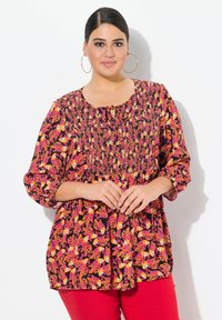 Blusa con stampa floreale che presenta un corpetto arricciato, scollo rotondo con dettaglio a fiocco e maniche 3/4 in tonalità vivaci di rosa, arancione e nero.
