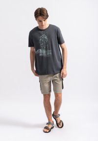 Donkergrijze graphic t-shirt met een wolkenontwerp. In combinatie met beige cargoshorts wordt de outfit compleet met bruine en grijze sandalen.