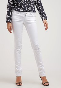 Jeans blancos ajustados con un corte delgado, diseño de cinco bolsillos y botones metálicos. Combinados con una blusa de manga larga floral en color azul marino.
