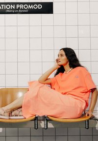 T-shirt corail vif et jupe ample assortie en tissu léger, avec un logo subtil et une finition lisse, assortis à des sandales à lanières.