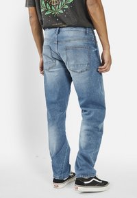 Ανοιχτό μπλε τζιν παντελόνι με άνετη εφαρμογή, που διαθέτει δύο πίσω τσέπες και διακριτικά σημάδια φθοράς. Συνδυάζεται με μαύρα και λευκά sneakers.