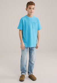 Svijetloplavi majica s kratkim rukavima s džepom na prsima, u kombinaciji s izblijedjelim trapericama i smeškim cipelama bez pertli. Jednostavan dizajn, opušteni kroj.