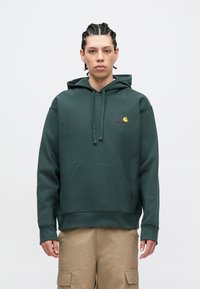 Sudadera con capucha verde oscuro hecha de mezcla de algodón. Cuenta con un bolsillo de canguro frontal, capucha con cordón y un pequeño logo en el pecho en amarillo y rojo.