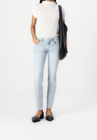 Ljusblå jeans med slim fit, i kombination med en kortärmad vit stickad tröja och svarta, platta skor med en dekorativ detalj.