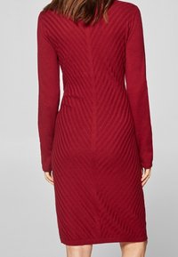 Rotes Strickkleid mit langen Ärmeln, einer figurbetonten Silhouette und strukturierten diagonalen Streifenmustern auf dem Rücken. Midikleid-Länge.