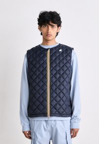 Navy quilted sleeveless vest with a zip closure featuring a yellow stripe and white logo accent. Worn over a light blue long-sleeve shirt.