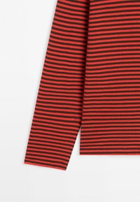 Długi rękaw z wąskimi czerwonymi i ciemnobrązowymi poziomymi paskami na białym tle.