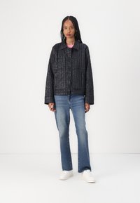 Svart quiltad jacka med ett strukturerat mönster, med två stora fickor och krage, matchad med ljusblå utsvängda jeans och vita sneakers.