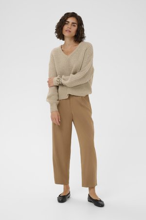 Beige knitted sweater with a V-neck, paired with light brown tailored pants. Black flats complete the outfit. Soft, textured fabric.