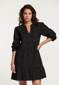 Rochie neagră cu mâneci trei sferturi, decolteu �în V, fustă în straturi și model brodat cu flori. Material moale cu detalii texturate subtile.
