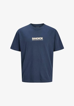 Veste verte surdimensionnée avec capuche, doublure grise, associée à un t-shirt bleu avec le texte "BANGKOK", jean bleu clair et baskets bleues.