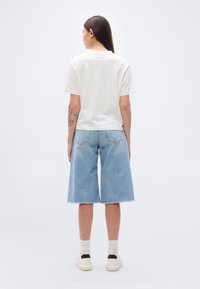 Λευκό βαμβακερό t-shirt, άνετη εφαρμογή, συνδυασμένο με ανοιχτό μπλε τζιν σορτς μέχρι το γόνατο, με ξεφτισμένο τελείωμα, λευκά αθλητικά παπούτσια με μαύρες λεπτομέρειες.