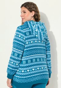 Felpa turchese realizzata in tessuto morbido, con motivi geometrici, cuori e fiocchi di neve in diverse sfumature di blu. Maniche e cappuccio aderenti.