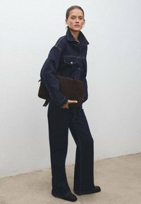 Chaqueta de mezclilla oscura y pantalones con un ajuste relajado, combinados con un bolso marrón texturizado. Superficie lisa con detalles de costura en contraste.