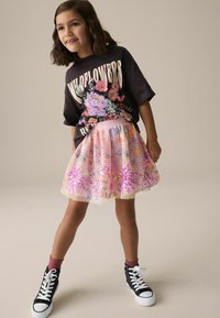 T-shirt graphique noir avec imprimé floral, associé à une jupe rose à volants ornée de sequins colorés et de broderies. Baskets montantes noires.