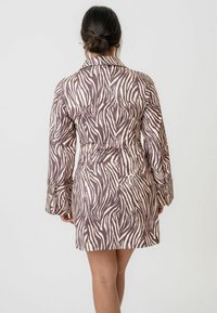 Rochie cu imprimeu de zebră în nuanțe de brown și bej, cu guler, mâneci lungi și talie ajustată, căzând deasupra genunchiului dintr-un material neted.